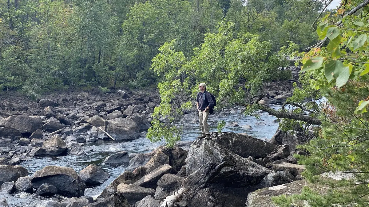 A man standing on top of rocks near water.